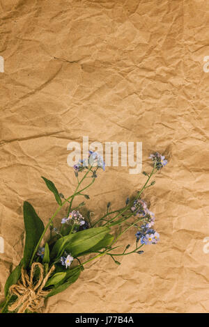 A bouquet of blue forget-me-not flowers on an old yellow rumpled parchment paper. View from above.. Stock Photo