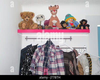 Shelf of cuddly toys in girl's bedroom with clothes hanging Stock Photo