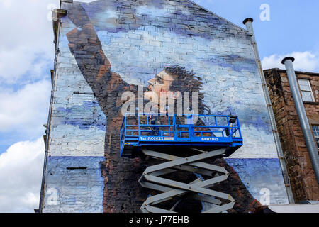 Glasgow, UK. 23rd May, 2017. 'Bob' the anonymous street artist, is putting the finishing touches to a 50 foot street mural of Billy Connolly, one of three, as part of Glasgow City's celebration of the world famous comedian's 75th birthday later this year. Billy is also being honoured by a tribute of portraits by Scottish artists John Byrne, Jack Vettriano and Racheal MacLean exhibiting in The Peoples Palace Museum in Glasgow Credit: Findlay/Alamy Live News Stock Photo