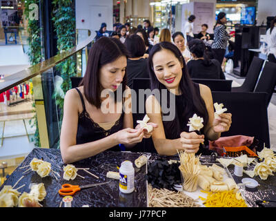 May 24, 2017 - Bangkok, Bangkok, Thailand - Women at the Emporium, an upscale shopping mall in Bangkok, look at the wooden roses they're making for the cremation of Bhumibol Adulyadej, the Late King of Thailand. In Thai culture it is customary to place wooden flowers in front of a deceased person's coffin or urn as a last tribute before cremation. The Royal Cremation Organisation Committee, which is overseeing plans for the cremation of Bhumibol Adulyadej, the Late King of Thailand, asked the Bangkok Metropolitan Administration (BMA) to provide three million wooden flowers for the late King's  Stock Photo