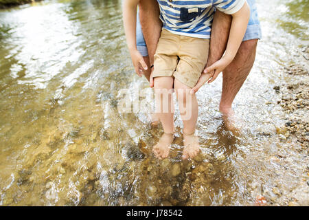 Unrecognizable father and son in the river, sunny day. Stock Photo