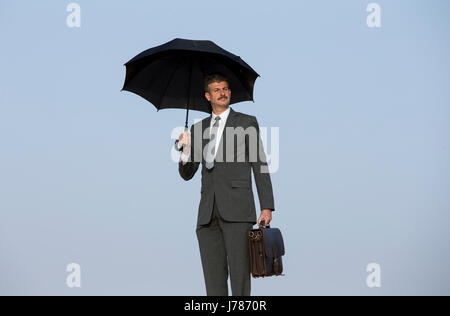 suited buisnessman in a desert with an umbrella Stock Photo