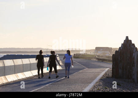 Women joggers enjoying the sun walking along the promenade of Camber Sands, East Sussex carrying water listening music talking jogging Stock Photo