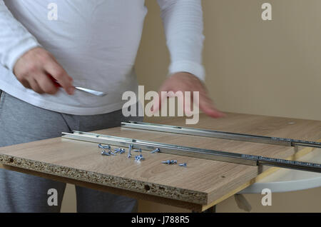Man in action - installing drawer slides with a screwdriver on an element of a cabinet in his apartment Stock Photo