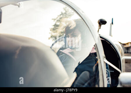 Smiling female pilot in the light aircraft cockpit, she is wearing aviator headset and checking controls Stock Photo
