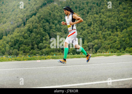 Rosa Khutor, Russia -  May 7, 2017: male runner running in compression socks on background of mountains and green trees in race Spring mountain marath Stock Photo