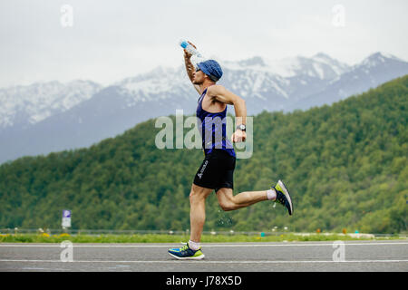 Rosa Khutor, Russia -  May 7, 2017: man runner on water point pours face from water bottle in race Spring mountain marathon Stock Photo