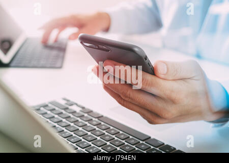 close up of businessman using mobile phone and laptop computer on white desk in modern office Stock Photo