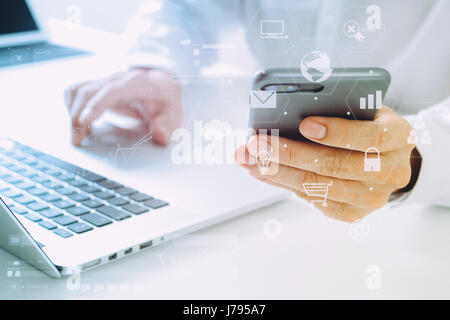 close up of businessman using mobile phone and laptop computer on white desk in modern office with VR icons diagram Stock Photo