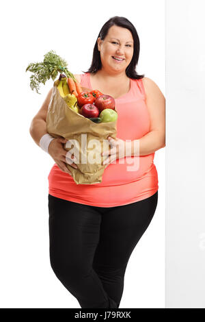 Woman with a bag filled with groceries leaning against a wall isolated on white background Stock Photo