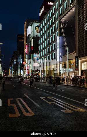 Nighttime photo of a busy downtown area showcasing night lights and pedestrians waiting or walking along the pavement or crossing the street. Stock Photo