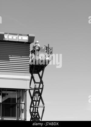 construction workers on mobile scissor lift installing cladding to new commercial warehouse development Stock Photo