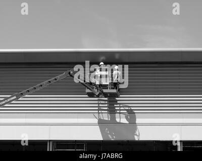 construction workers on mobile access platform installing on cladding to new commercial warehouse development Stock Photo