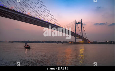 Vidyasagar Setu bridge at twilight with a wooden boat on river Hooghly.