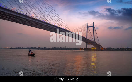 Vidyasagar Setu bridge at twilight with a wooden boat on river Hooghly.
