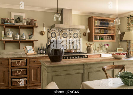Old Minton tiles above range cooker in elegant and cosy kitchen with waxed pine units and butchers island. The pendant lights are from Hector Finch Stock Photo