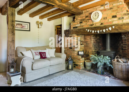 Cosy sitting room with inglenook fireplace, exposed brick wall and wood beamed ceiling. The cream sofa is from Laura Ashley and the rug from John Lewi Stock Photo