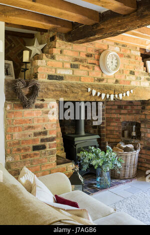 Cosy sitting room with inglenook fireplace, exposed brick wall and wood beamed ceiling. The cream sofa is from Laura Ashley and the rug from John Lewi Stock Photo