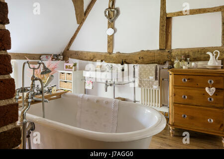 Vaulted bathroom with ancient beams, exposed brick wall and roll-top French bath. Stock Photo