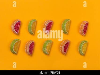 Still life of colored lobules of marmalade lying in two rows on an orange background Stock Photo