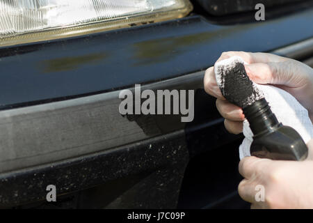 The man's hands apply a plastic paste to a white cloth. Man's hand puts a paste on the black weathered plastic bumper of a car. Stock Photo