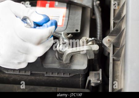 The hands of the car mechanic in disposable gloves unscrew the battery clutch. The hand of a mechanic with a flat key unscrews the battery in the car. Stock Photo