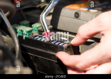 The mechanic inserts a new fuse into the socket using the pliers. The hands of the mechanic replacing the fuse in the car. Stock Photo
