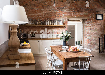 Exposed brick wall in contemporary feeling kitchen with farmhouse wooden table Stock Photo