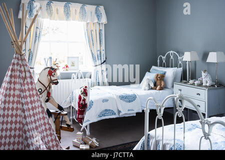 Childs bedroom with twin iron beds, old fashioned rocking horse and curtains from House of Curtains. The walls are painted in Parma Gray by Farrow & B Stock Photo