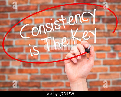 Man Hand writing Consistency is The Key with black marker on visual screen. Isolated on bricks. Business, technology, internet concept. Stock Photo Stock Photo