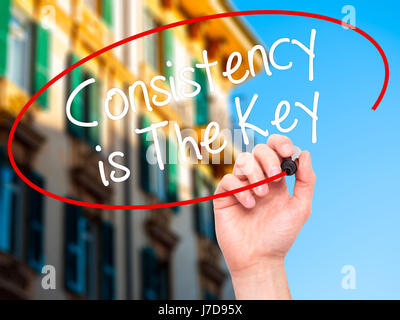 Man Hand writing Consistency is The Key with black marker on visual screen. Isolated on city. Business, technology, internet concept. Stock Photo Stock Photo