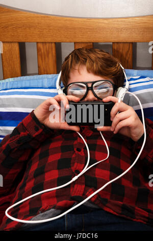 11-year old boy in bedroom using a smartphone to surf the web Stock Photo