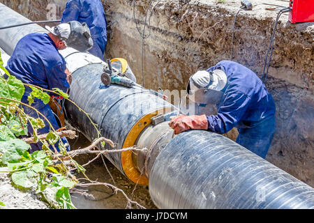 Team of welders is in trench working hard to install a new pipeline. Arc welding pipes Stock Photo