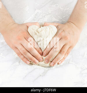 A man's hands kneading dough in the form of a heart, with flour on a marble table, with a place for text, square photo Stock Photo