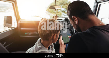 Close up rear view of father and son looking at map on digital tablet while travel by car. Family looking for road on map. Stock Photo