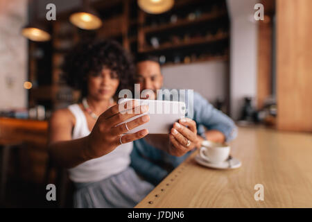 Close up of female hands holding mobile phone and taking self portrait. Young woman taking selfie with smart phone while sitting at cafe with her boyf Stock Photo