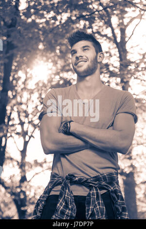 one young man, smiling, upper body shot, outdoors park nature tree branches, sunny day, duotone, black and white image Stock Photo