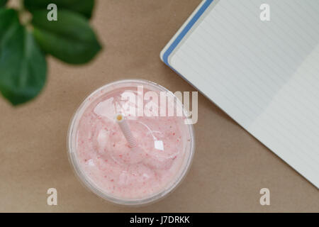 Top view of a strawberry smoothie in a plastic cup with a straw on the table with notebook. Summer and healthy lifestyle concept. Stock Photo
