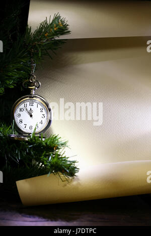 New Year decoration. Vintage pocket watch hanging near firtree against blank scroll Stock Photo