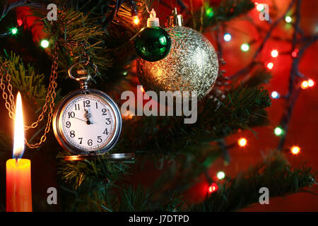 Vintage pocket watch hanging on Christmas tree near lighting candle Stock Photo