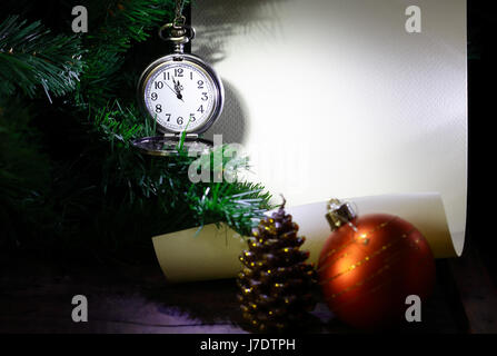 New Year decoration. Vintage pocket watch hanging near firtree against blank scroll Stock Photo