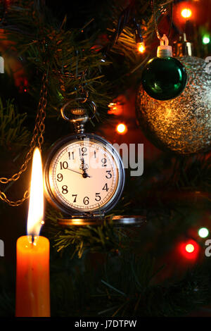 Vintage pocket watch hanging on Christmas tree near lighting candle Stock Photo