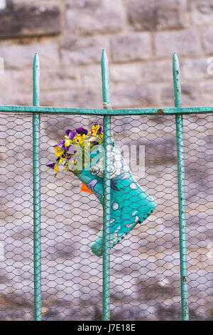 Childs wellington boot used as a flower pot full of pansies hanging on a metal fence. UK Stock Photo