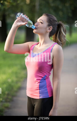 Thirsty woman drinking water to recuperate after jogging Stock Photo