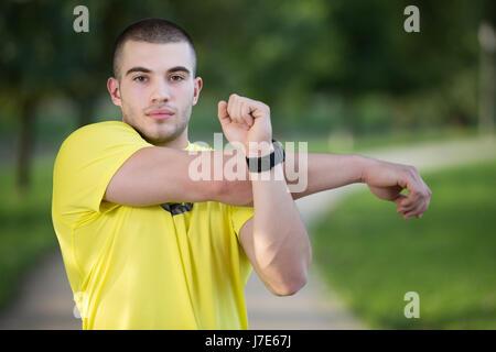 Fitness man stretching arm shoulder before outdoor workout. Sporty male athlete in an urban park warming up. Stock Photo