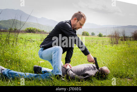 The crime scene, murder, investigation, police caught the killer and detained, killer lying on the grass with his hands behind his back, his cop with  Stock Photo