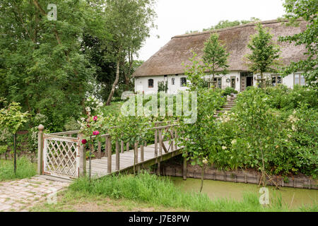 Gated footbridge and garden of thatched 17th century famhouse built on 12th century earthmound to prevent flooding Stock Photo