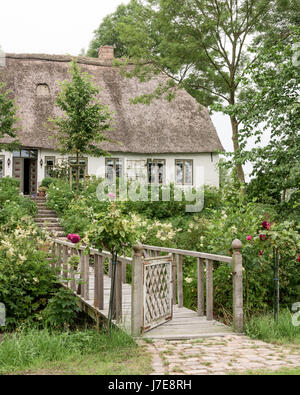 Gated footbridge and garden of thatched 17th century famhouse built on 12th century earthmound to prevent flooding Stock Photo