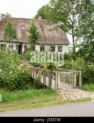 Gated footbridge and garden of thatched 17th century famhouse built on 12th century earthmound to prevent flooding Stock Photo