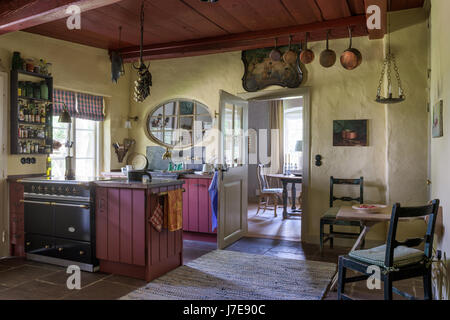 Pair of old English chairs with Swedish rag rug in kitchen with oval framed internal window above Belgian bluestone sink Stock Photo